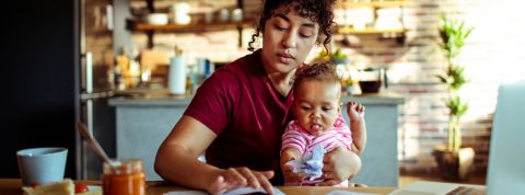 Une femme travaillant sur son ordinateur avec un enfant dans les bras