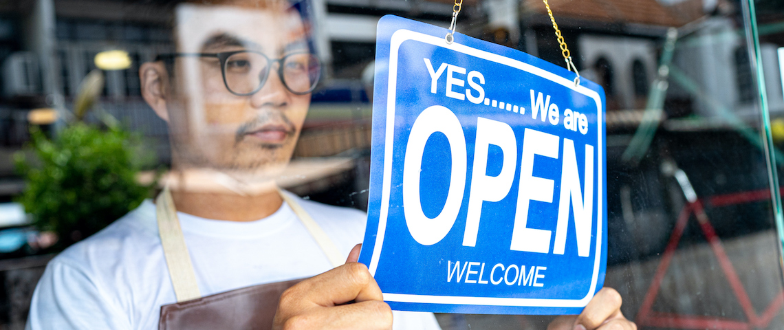 Un jeune homme portant des lunettes et un tablier ouvre sa boutique