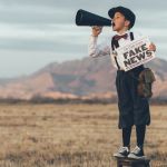 Un enfant avec un mégaphone et un journal où il est écrit Fake News