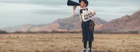 Un enfant avec un mégaphone et un journal où il est écrit Fake News