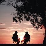deux jeunes qui parlent assis face au coucher du soleil