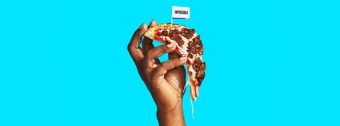 Une main qui tient une pizza avec de la viande végétale sur un fond bleu