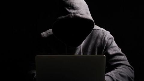 Un homme avec une capuche dans le noir devant son ordinateur
