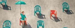 Jeune femme blonde tenant un parasol turquoise sur une plage, assise à travers de nombreuses chaises rouges et sarcelles dans le sable, par une journée ensoleillée