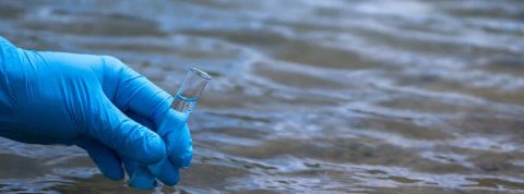 La main d’un homme dans un gant bleu prend un gros plan d’eau dans un tube à essai pour mesurer la pollution de l’eau