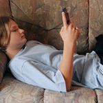 une ado allongée sur un canapé regarde son téléphone
