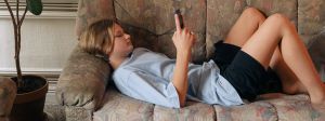une ado allongée sur un canapé regarde son téléphone