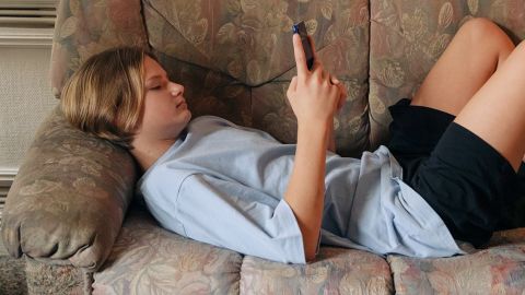 une ado allongée sur un canapé regarde son téléphone