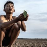 Jeune homme asiatique accroupi sur une terre craquelee regarde le ciel