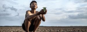 Jeune homme asiatique accroupi sur une terre craquelee regarde le ciel
