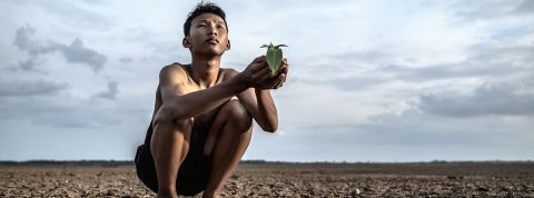 Jeune homme asiatique accroupi sur une terre craquelee regarde le ciel