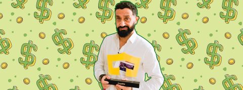 Hanouna souriant, portant un trophée Royaltiz sur fond de dollars