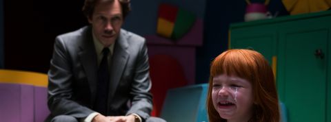 Un petite fille pleure avec un homme au second plan, dans la pénombre