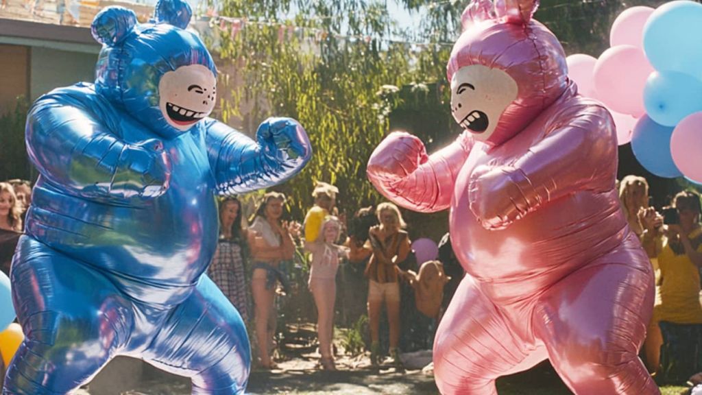 Deux personnes déguisées en bébé bleu et rose boxent dans un jardin