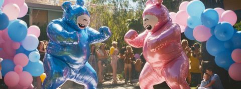 Deux personnes déguisées en bébé bleu et rose boxent dans un jardin