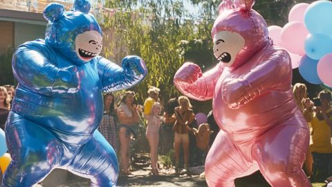 Deux personnes déguisées en bébé bleu et rose boxent dans un jardin