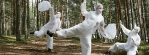 3 personnes en forêt dansent en combinaisons blanches en ramassant des déchets