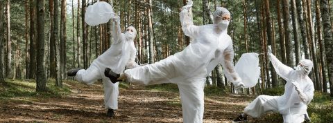3 personnes en forêt dansent en combinaisons blanches en ramassant des déchets