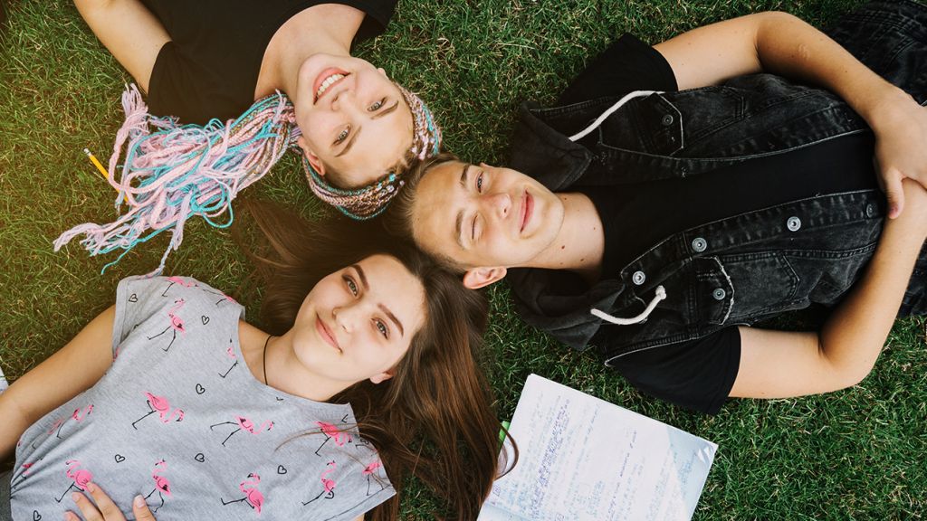 Des adolescents joyeux allongés sur l'herbe avec leurs cahiers ouverts