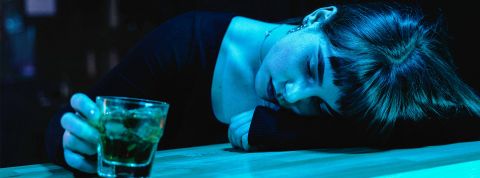 Une jeune femme avec un verra à la main effondrée sur un bar
