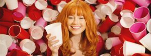Une jolie femme rousse entourée de gobelets en plastique de couleurs