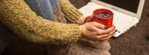 Une femme avec gros pulle et grosses chaussettes tient un mug de thé brûlant pour se réchauffer