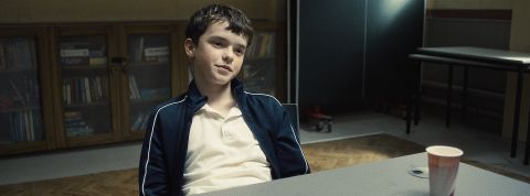 une jeune garçon assi. à une table l'air sur de lui.
