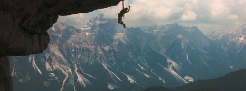 Un homme suspendu dans le vide, accroché à la montagne (image du film Cliffhanger)