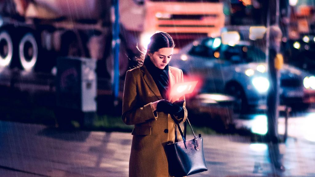 Une femme regarde son telephone dans la rue en soirée