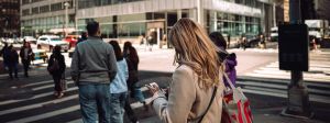 Une femme blonde de dos les yeux rivés sur son smartphone au passage piéton